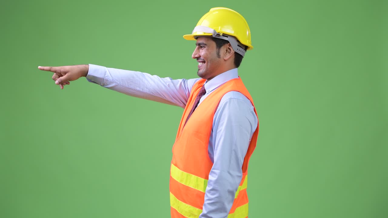 Profile view of young handsome Persian man construction worker pointing finger