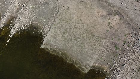 flight with a drone in ascent with a top-down view and with a turn on the shore of a reservoir seeing the remains of a stone structure scattered in the water and three people walking winter spain