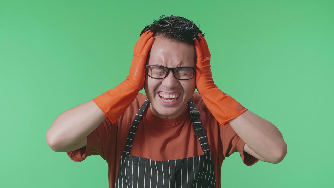 후회로 가까운 아시아 남성 집주인이 머리를 잡고 초록색 스크린 스튜디오에 서서 소리를 지르고 있습니다.