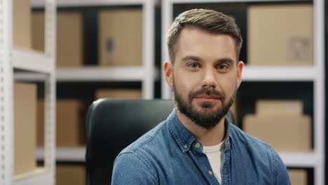 portrait of handsome young male postman smiling cheerfully to camera in postal storage of parcels