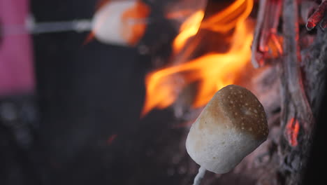 Low-angle-close-up-of-marshmallows-roasting-on-metal-sticks-over-campfire