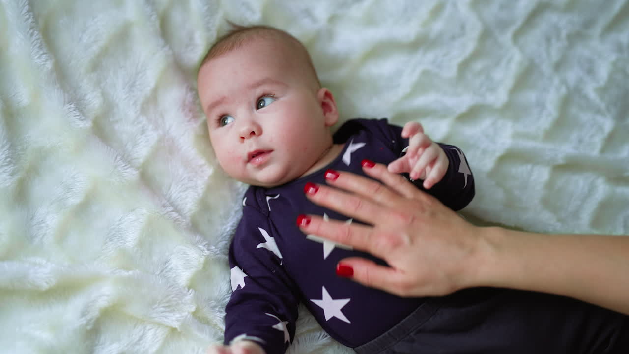 Mommy playing with her baby boy. Caring mum touches her son's belly shaking him sweetly. Top view. White backdrop.