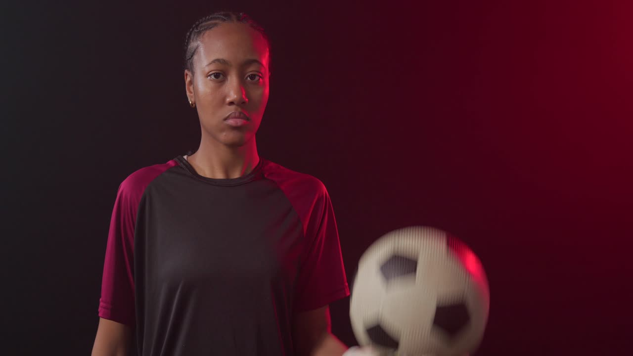 Portiere donna afroamericana che bilancia un pallone da calcio, facendolo ruotare e cullandolo, mostrando controllo sotto un bordo rosso