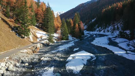 vuelo hacia adelante sobre un pequeño río en el parque nacional suizo, con algo de nieve en el suelo y hermosos árboles de colores otoñales