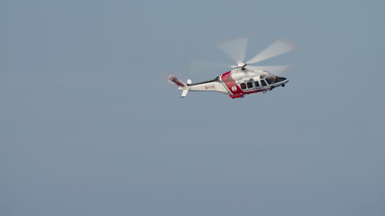 Rød og hvid kystvagtshelikopter flyver på blå himmel