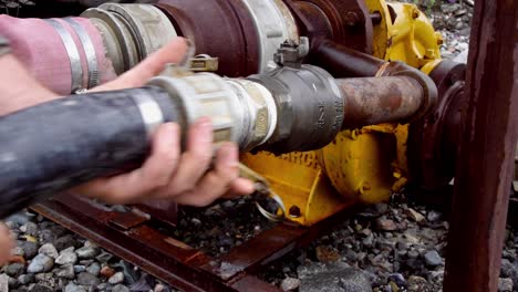 Strong-Caucasian-male-hands-remove-commercial-hose-from-industrial-fitting-from-equipment-on-rocky-stone-ground,-static-close-up-profile