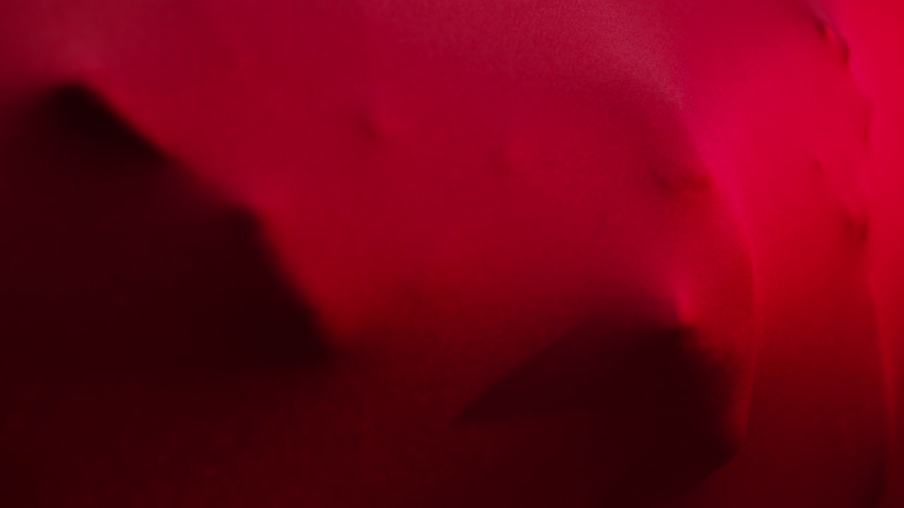 Un sorprendente scatto artistico di un volto e mani che emergono da un drappo rosso fluente, creando un'atmosfera misteriosa e surreale. L'illuminazione drammatica e il vivido contrasto di colori mettono in risalto l'emozione, la texture