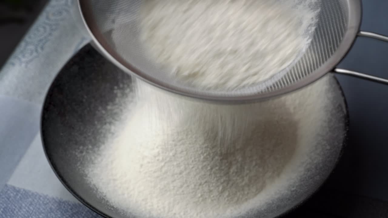 Young Girl Sifts Flour Through a Sieve into a Baking Dish, Close-up View