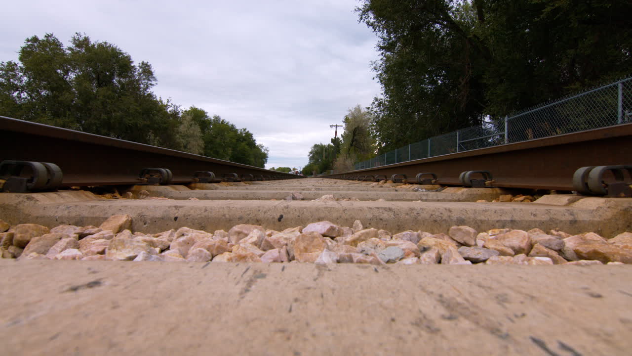 A camera situated on the middle of the train tracks films a low angle of a commuter train as it passes overhead during a cloudy day.