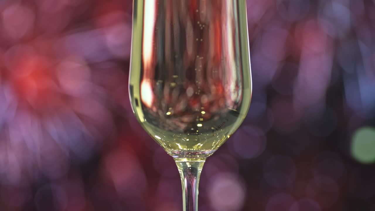 Un primo piano di un flûte di champagne pieno di spumante, illuminato su uno sfondo bokeh di fuochi d'artificio.