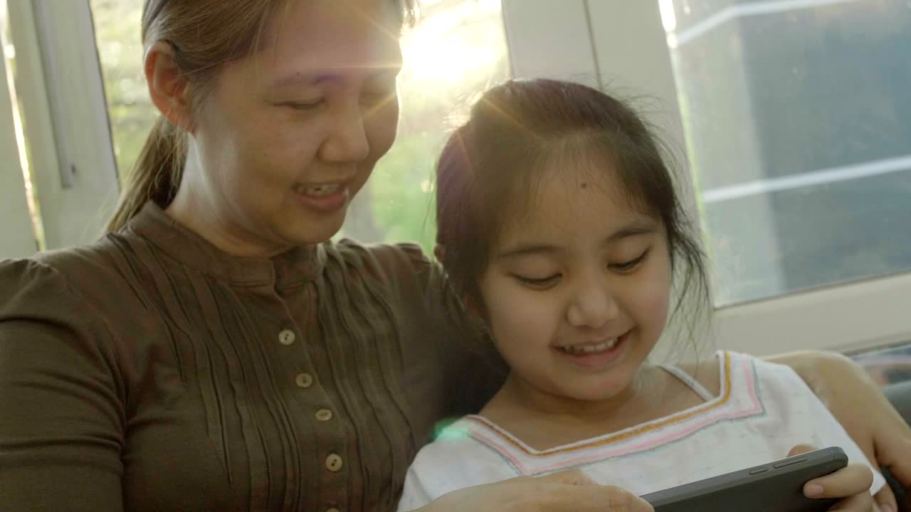4k 아시아 소녀가 어머니와 함께 스마트폰에서 게임을 하고 행복한 시간을 보내고 있습니다.