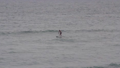 long shot, a man doing stand up paddle in the caribbean ocean cloudy