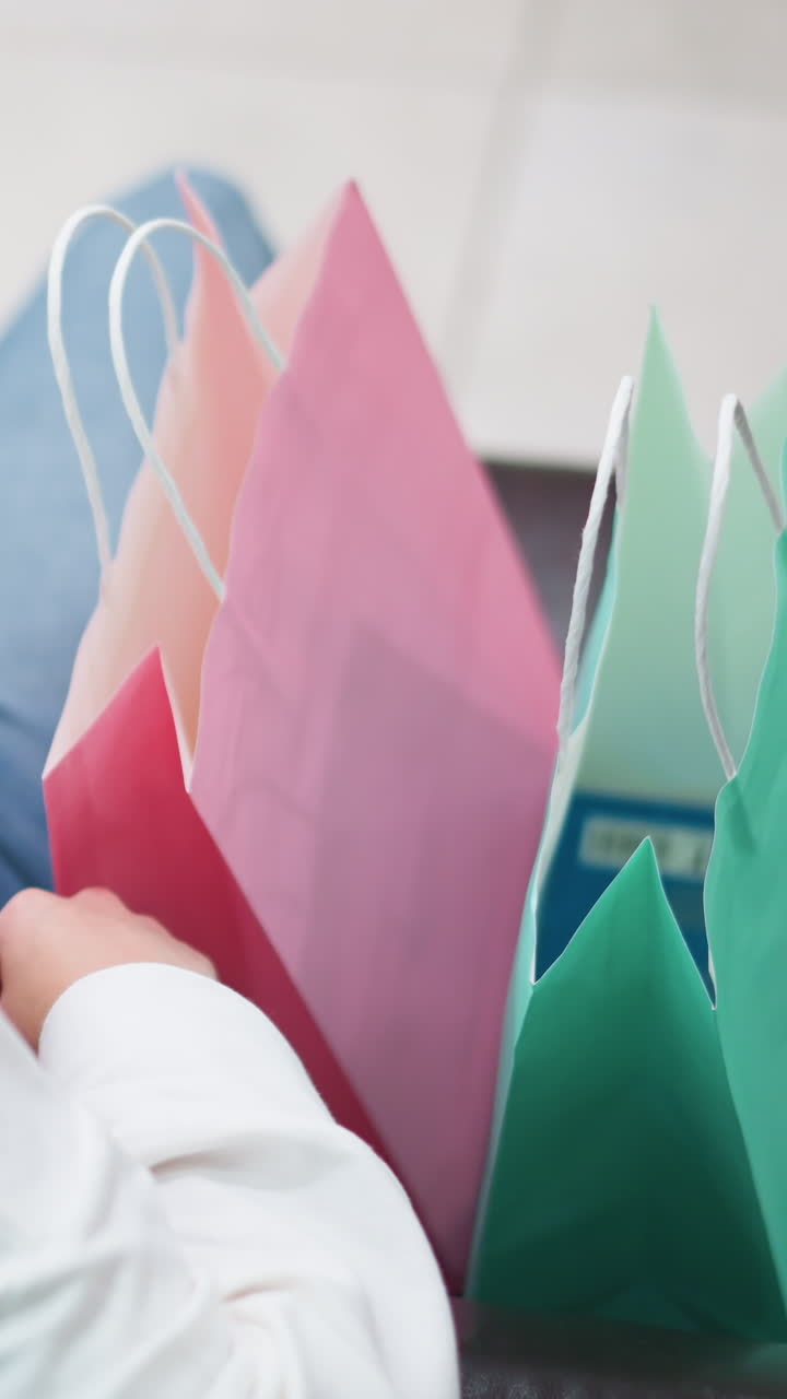 vista trasera de la dama sentada en el sofá sosteniendo bolsas de compras de diferentes colores, ajusta su cabello, bolsas de rosa, verde y azul se colocan en su regazo mientras se relaja