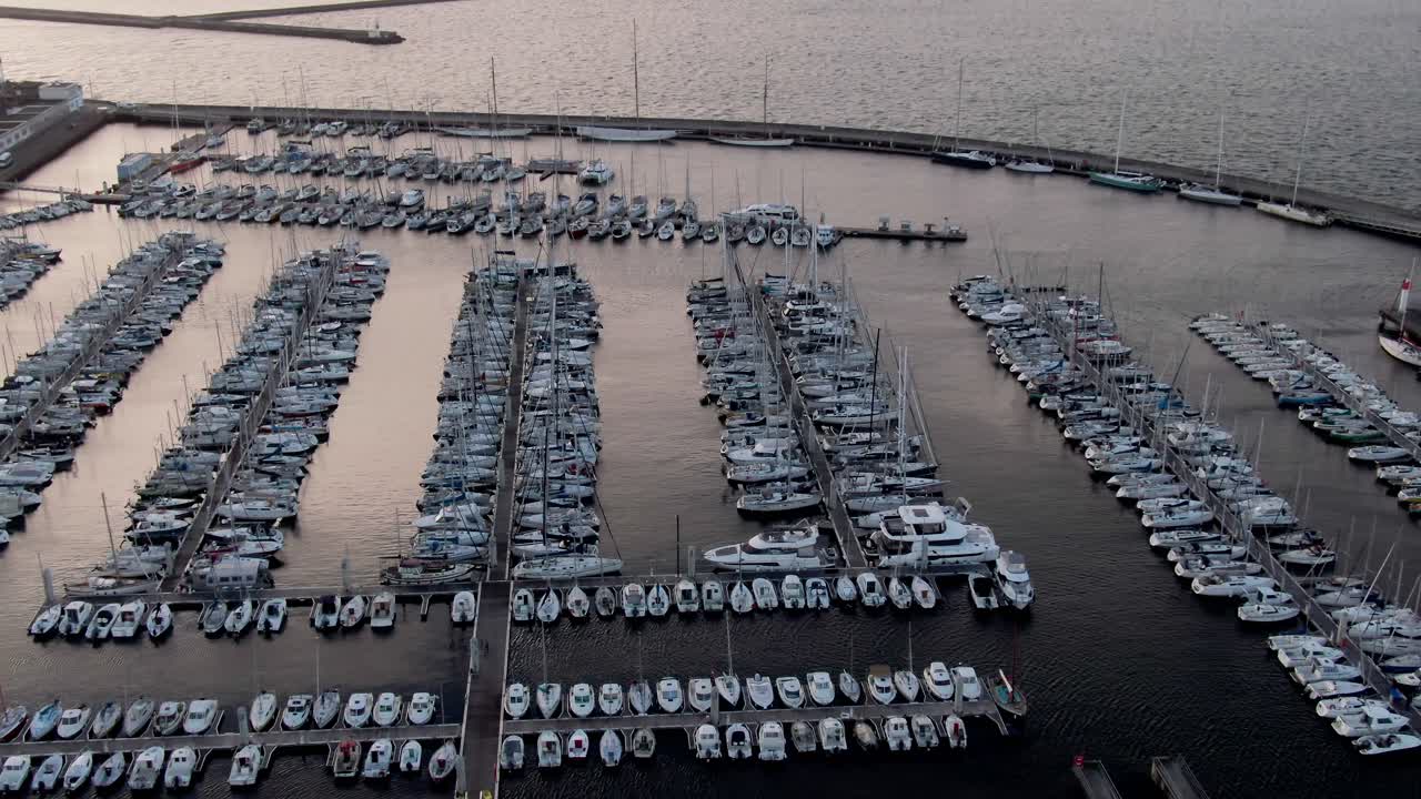 När solen går ner närmar sig en drönare en marina, målar himlen och vattnet med varma nyanser och fångar en fridfull kustscen.