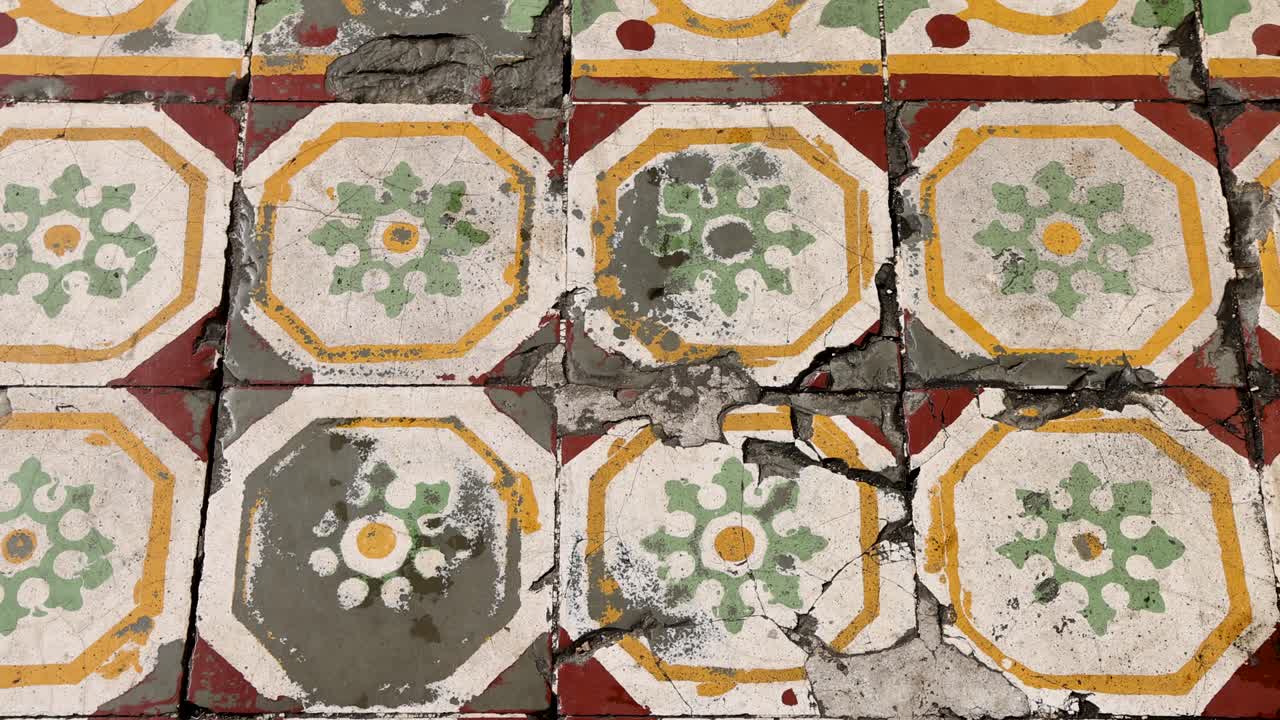 A sequence shows the gradual repair of cracked, ornate floor tiles with cement, under natural daylight, using a steady overhead camera angle