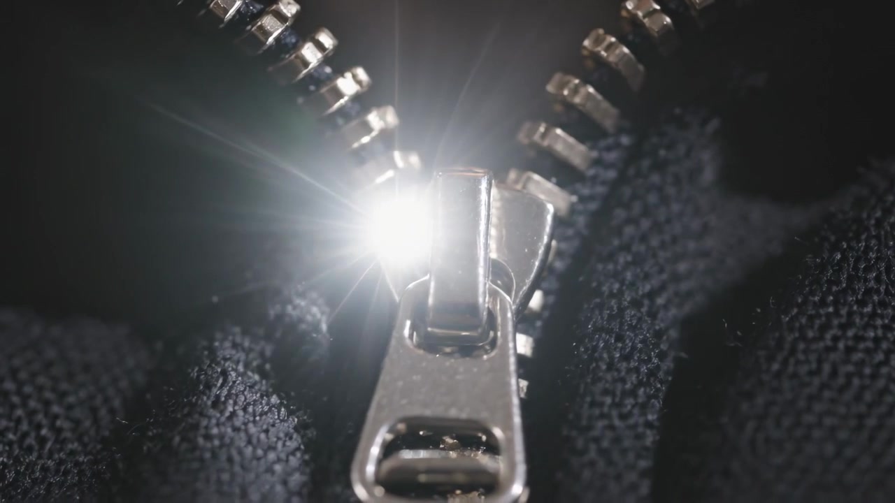 Glijdende metalen ritssluiting gaat omhoog op jas na het sluiten van kledingstuk, treklipje en licht zichtbaar.