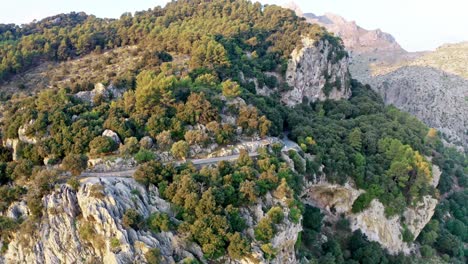 steep road on the edge of a mountain range on sunny day, rotate drone shot