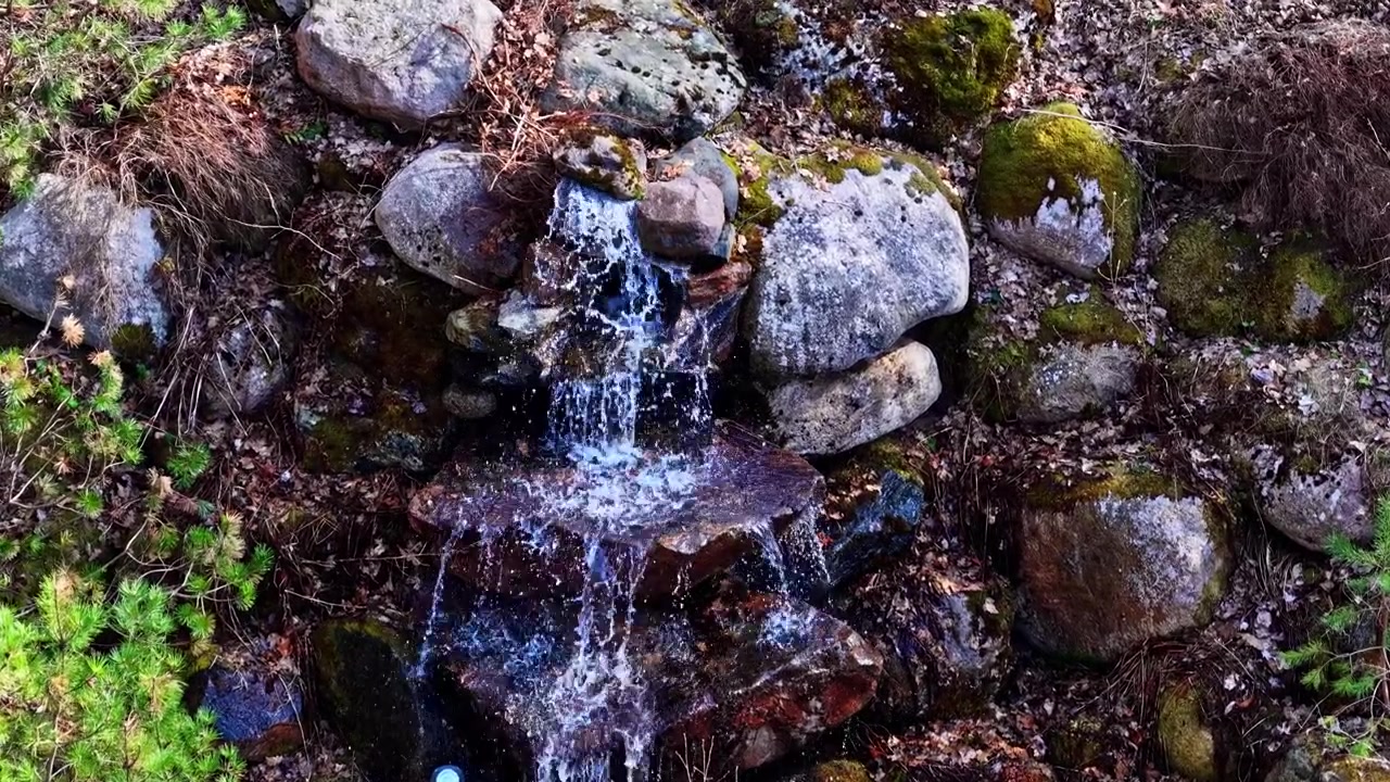 Clear water flows over mossy rocks in a small natural outdoor waterfall scene