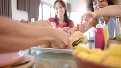 diverse friends reaching for sandwiches, enjoying meal together at home gathering