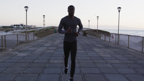 hombre afroamericano enfocado haciendo ejercicio al aire libre, corriendo por la orilla del mar