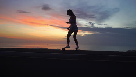 beautiful girl rides a skateboard on the road against the sunset sky