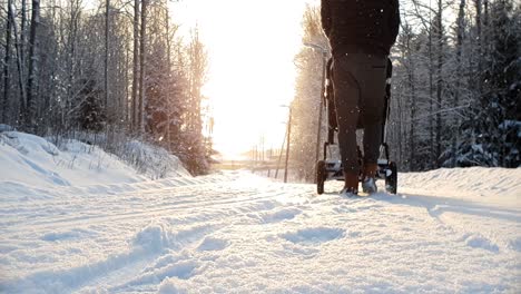 Static-slow-motion,-father-walking-with-baby-stroller-in-snowy-winter-weather-at-golden-sunset