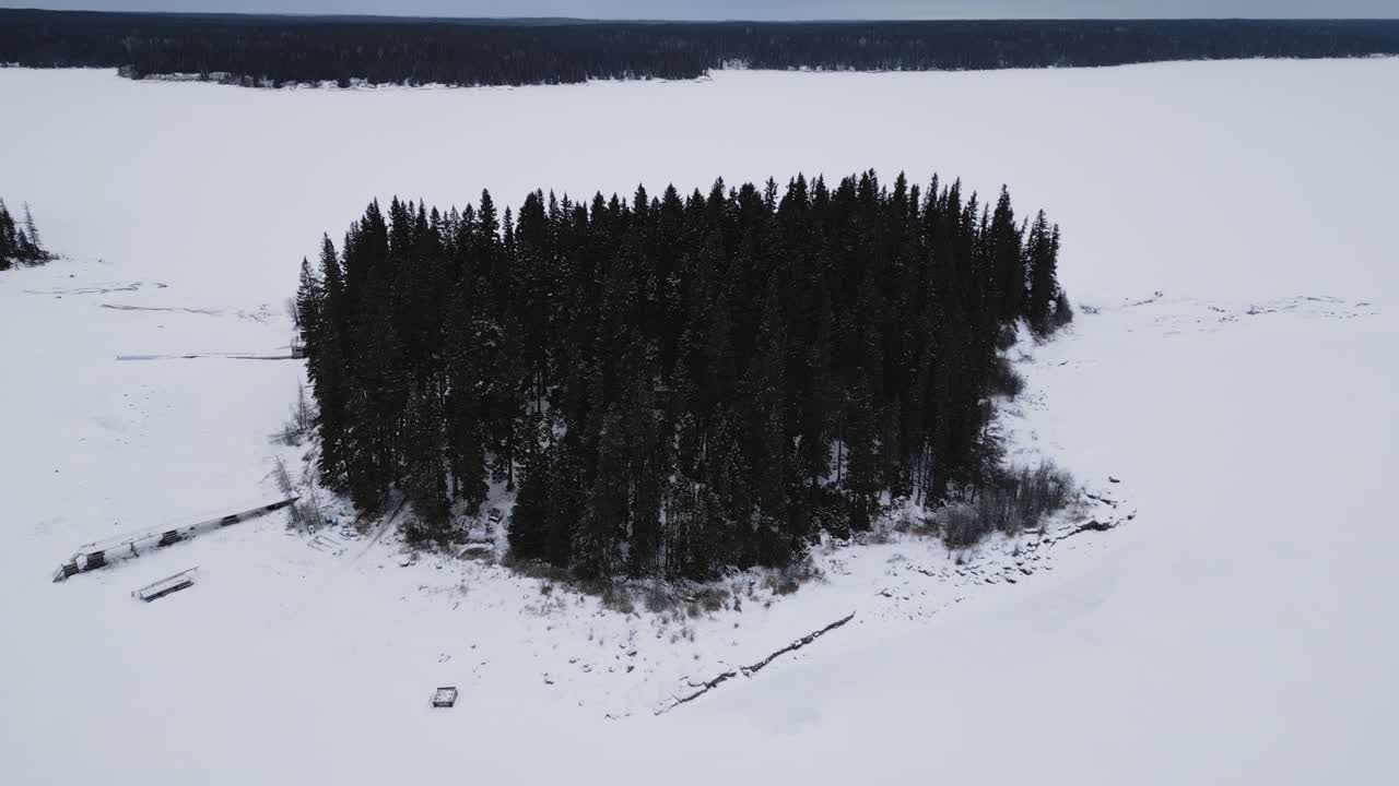 Ripresa aerea con drone in discesa di un'isola sul lago ghiacciato canadese Paint Lake con una capanna da pesca sul ghiaccio e motoslitte.