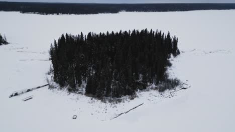 A-lowering-Drone-Shot-of-an-Island-on-Frozen-Canadian-Paint-Lake-with-an-Ice-fishing-hut-and-skioos