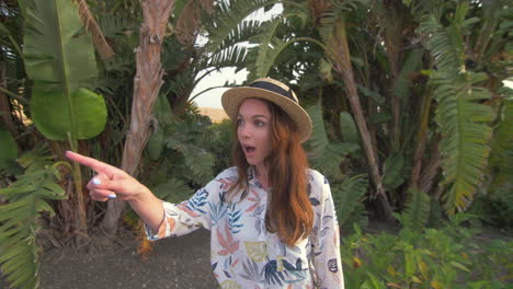 a woman smiles and points excitedly while standing in a tropical garden.