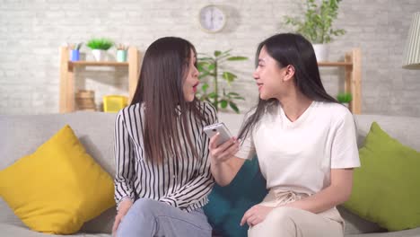 two happy young asian woman use their smartphone sitting on the sofa in the living room