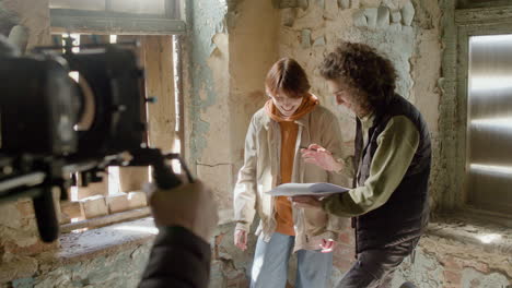 colleghi che leggono una sceneggiatura in un edificio in rovina mentre vengono registrati da un cameraman