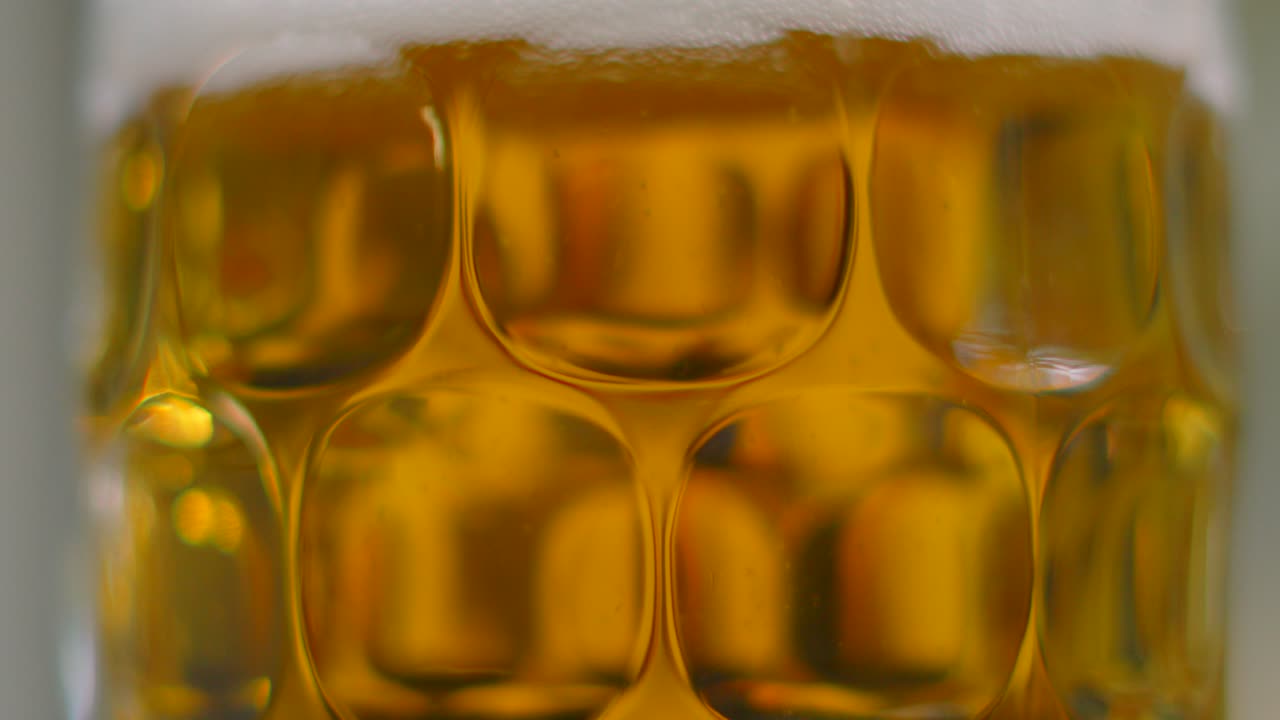 Inquadratura dall'alto di una birra chiara appena versata in un bicchiere tradizionale, con un colore arancione vivido e schiuma bianca in superficie