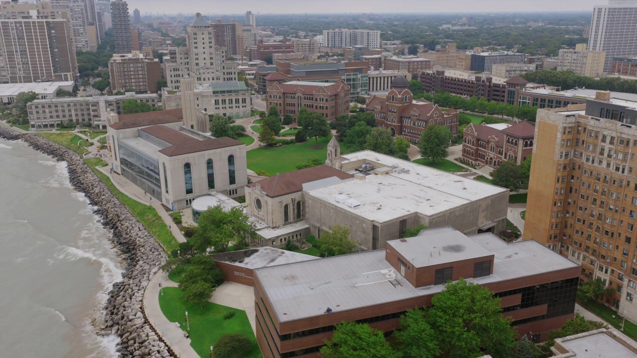 Ripresa aerea con drone di un campus universitario lungo la costa del lago Michigan a Chicago, con edifici accademici e lo skyline della città sullo sfondo