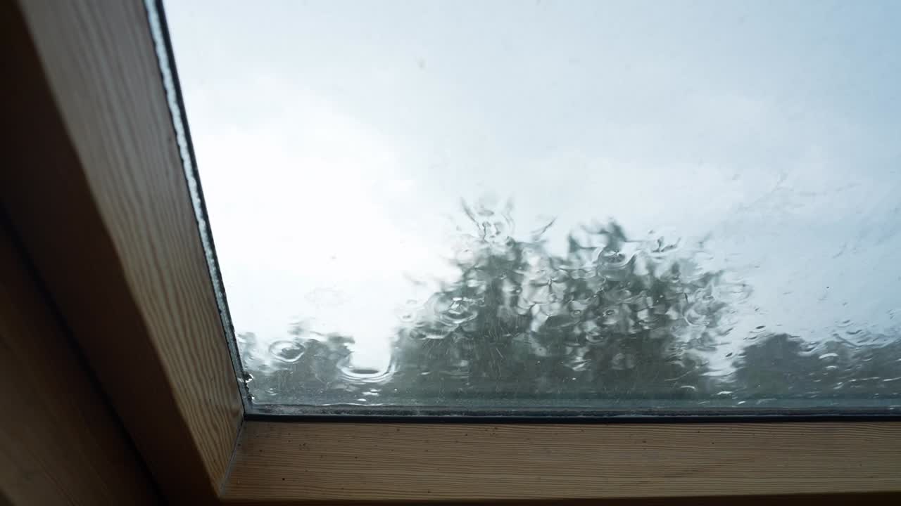 Close-up view of raindrops hitting and streaming down a window from the interior perspective