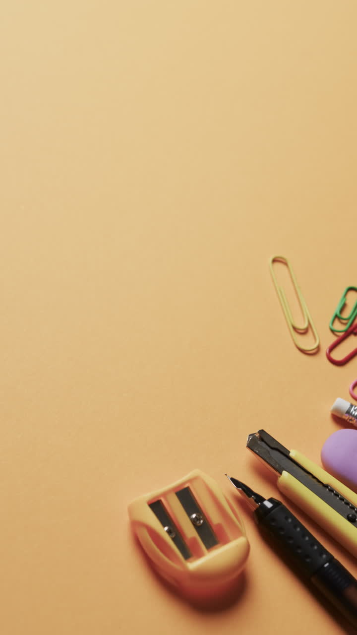 Vertical video of overhead view of school stationery on beige background, in slow motion