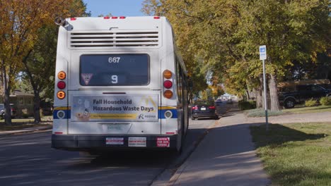 un autobús urbano sale de una parada de autobús y se dirige por la calle durante un hermoso día de otoño