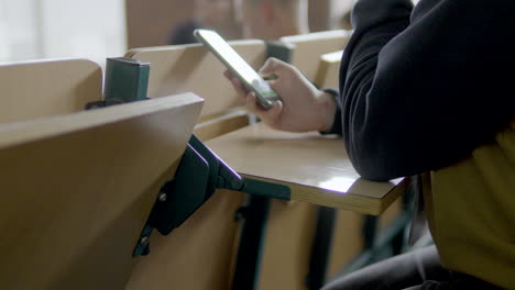 un hombre en una sala de conferencias apoya su teléfono en una mesa plegable contra el respaldo de una silla - de cerca