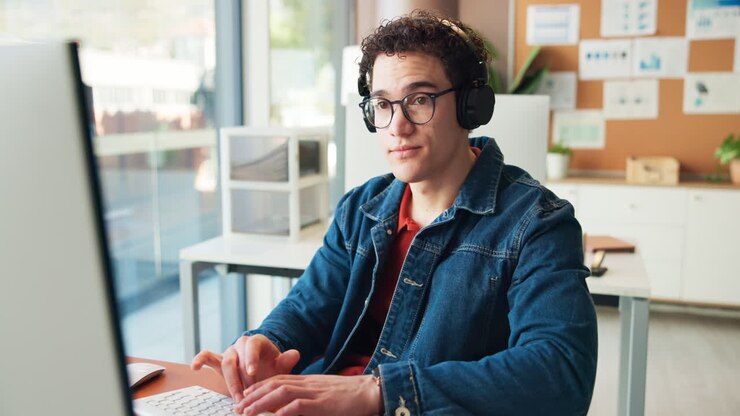 Young Man Wearing Headphones Working on Computer in Modern Office