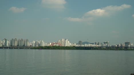 Nicht-Erkennbare-Person-Wasserski-Auf-Dem-Fernblick-Des-Hangang-flusses,-Autoverkehr-Auf-Der-Seogang-brücke,-Gangbyeon-schnellstraße,-Mapo-gu-wohngebäude-Und-Seoul-Namsan-turm-Hinter-Der-Insel-Bamseom