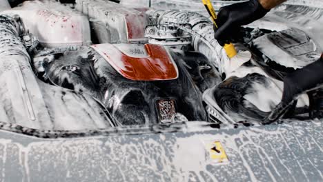 man with black latex gloves cleaning the engine bay of a ferrari with a brush in slow motion