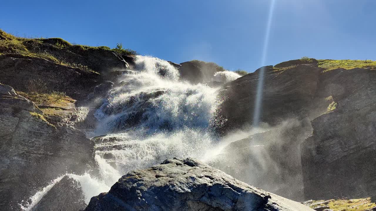 mirando hacia la hermosa cascada de montaña limpia noruega en vikafjell voss noruega - sol de verano con rayos de sol y fondo de cielo azul y agua salpicada por todas partes - portátil estático
