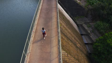 shot from a drone of a woman walking on the top of a dam and look at the reservoir during the day