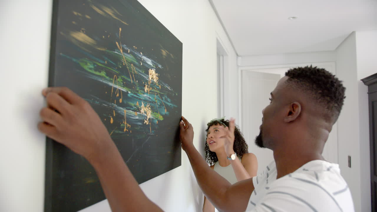 Hanging abstract painting on wall, couple decorating home together, enjoying art