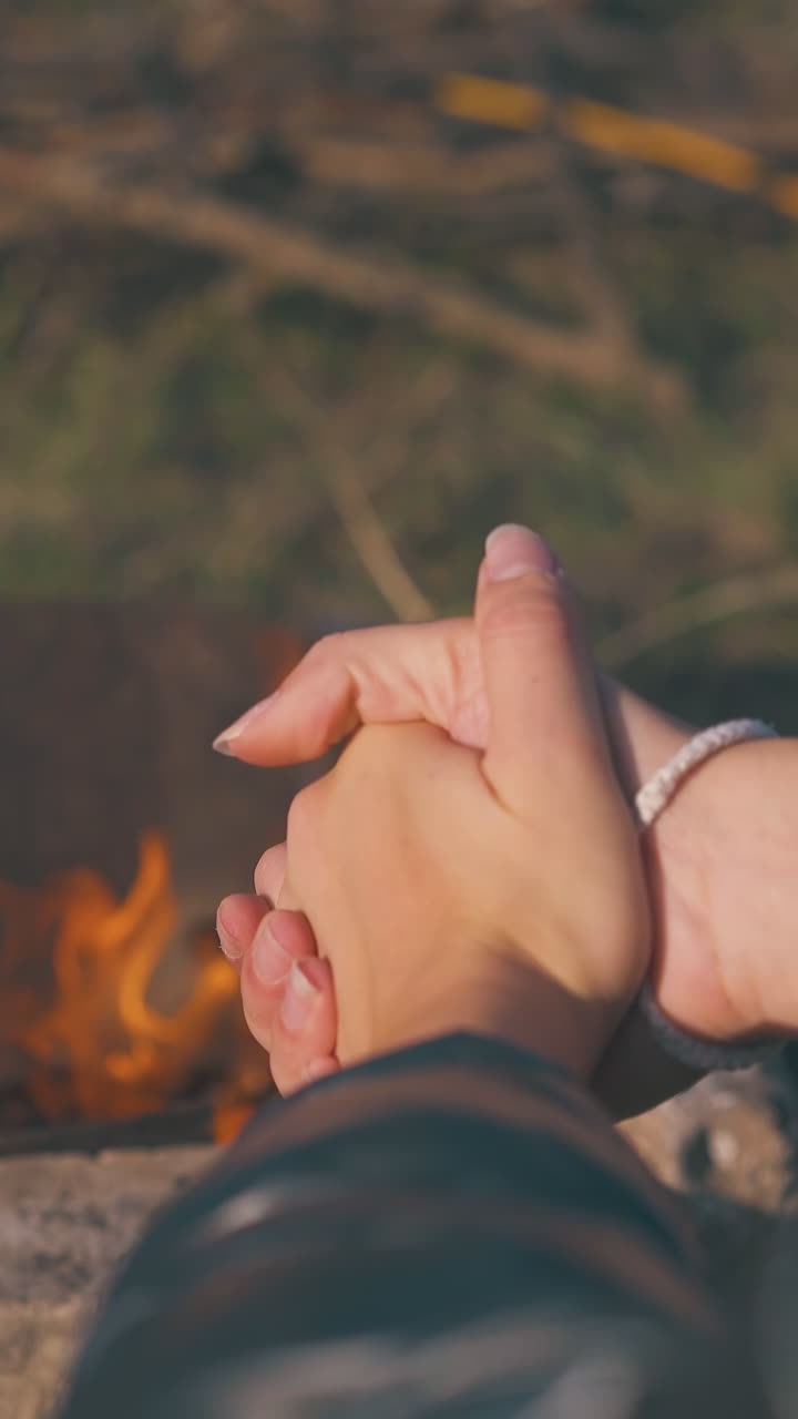 girl tourist heats hands at burning bonfire surrounded by stones at camp in autumn morning backside view closeup
