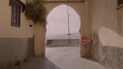 Wide-shot-of-horse-shoe-arch-in-Moroccan-street-Medina,-with-motorcycle-and-car-driving-in-frame