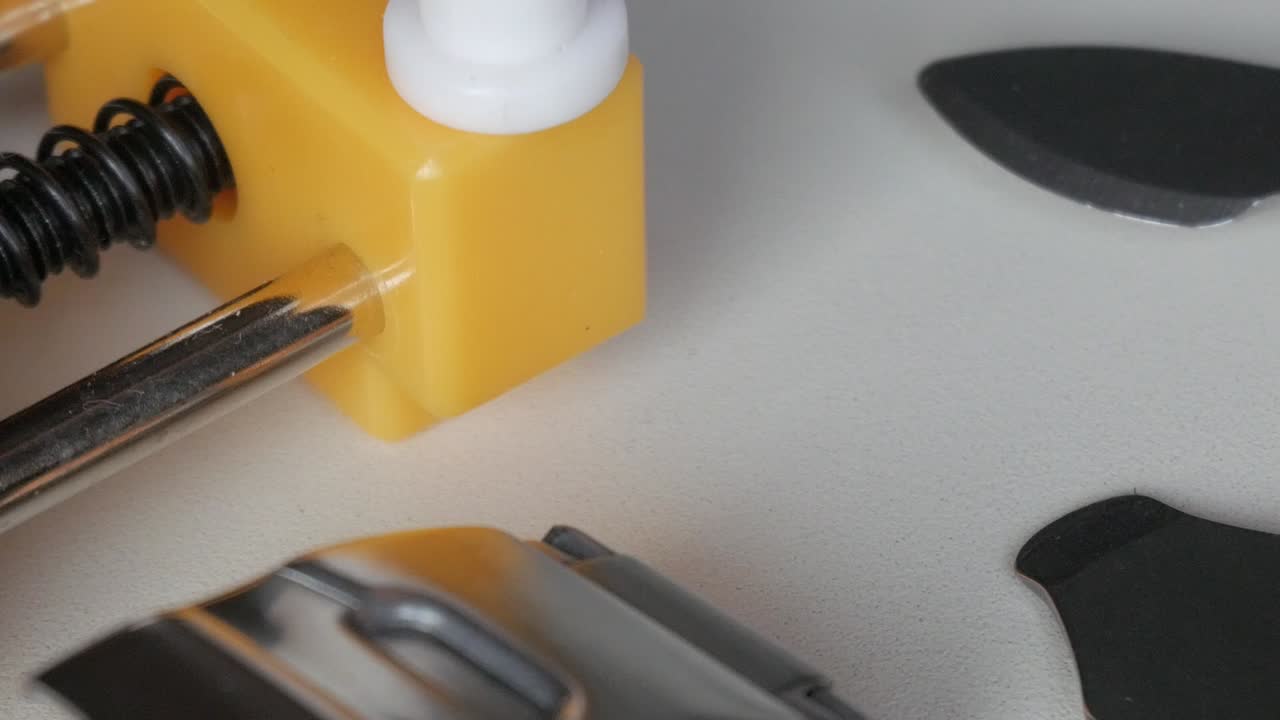 Vista dettagliata di uno strumento giallo per la riparazione di orologi con un meccanismo a molla visibile, in panoramica verso destra