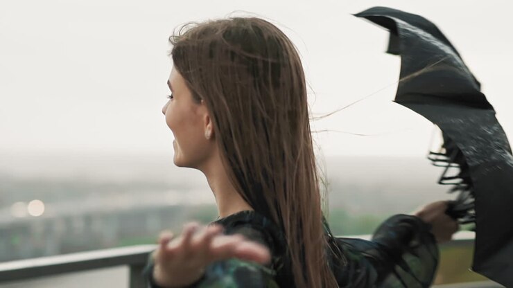 Donna gioiosa con ombrello nero volteggia sotto la pioggia primaverile.