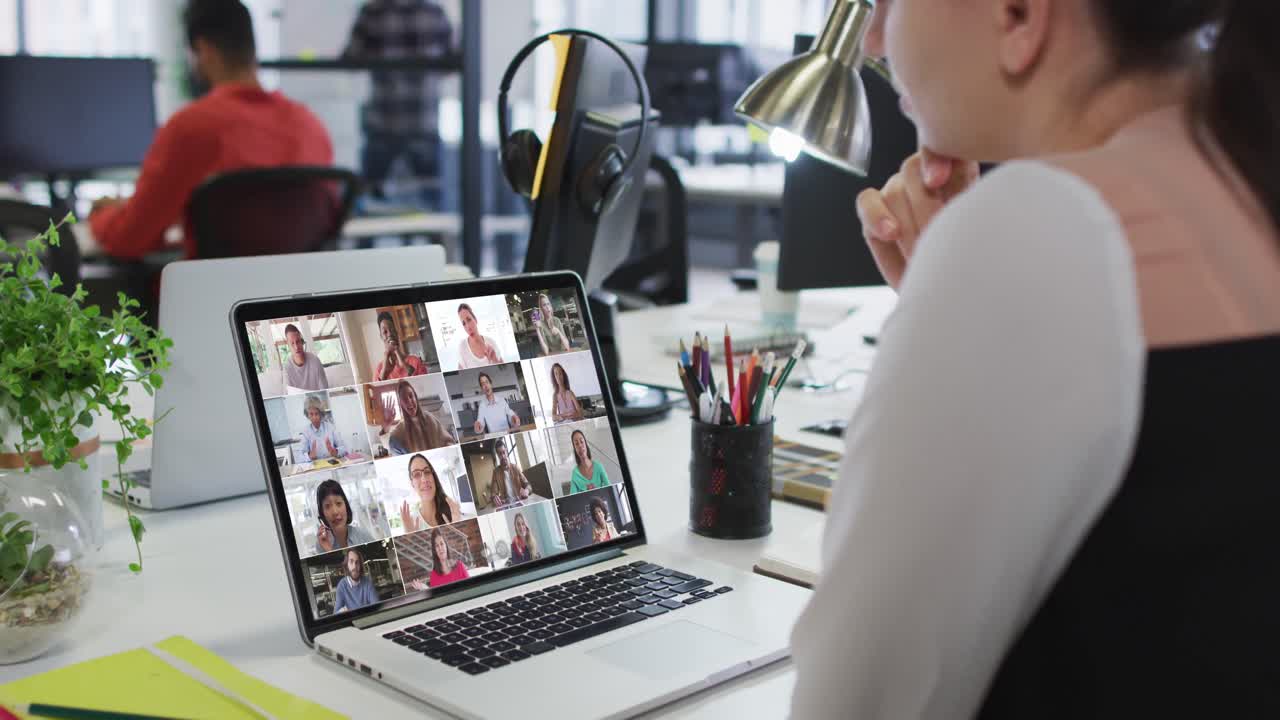 Kaukasisk kvinde deltager i videokonference med kontorkolleger på bærbar computer på kontoret.