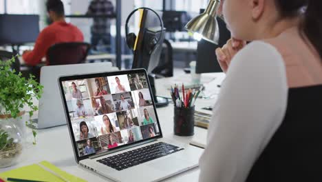 mujer caucásica teniendo una videoconferencia con colegas de oficina en una computadora portátil en la oficina
