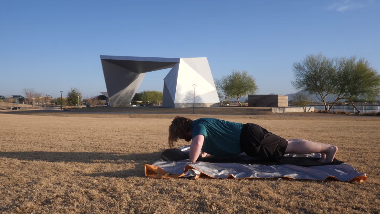 Red hair male doing push ups in a park with an amphitheater behind them.